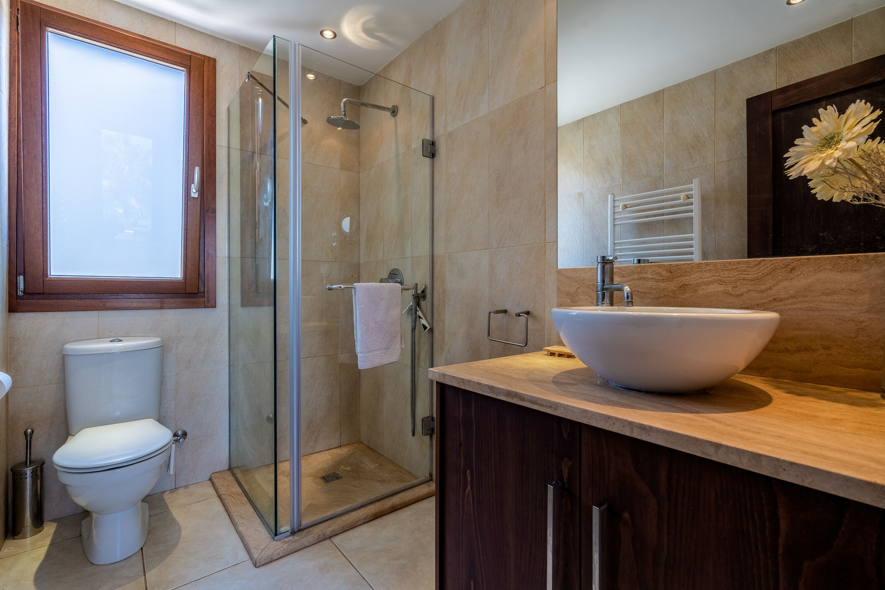 Ein modernes Badezimmer mit Duschkabine aus Glas, einer weißen Toilette und einem Holzwaschtisch mit großem, weißem Becken.
