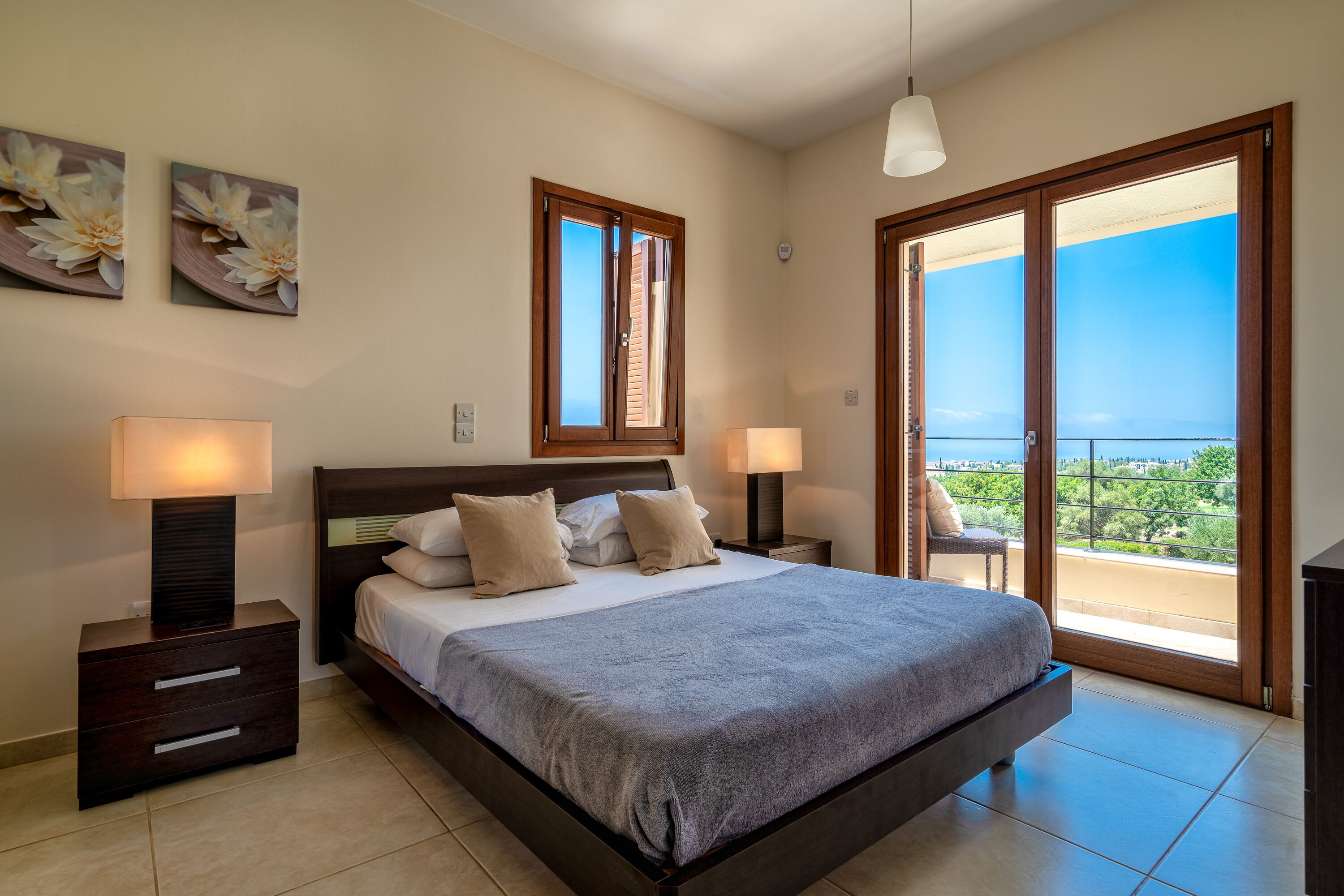 A bedroom with a large bed, two bedside tables with lamps, a window with a view, and a ceiling light.