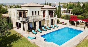 Una casa de dos pisos con piscina, mobiliario exterior y vistas a parques eólicos al fondo.
