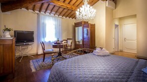 A bedroom with a bed, a TV, a wooden dresser, a chandelier, and a mirror.
