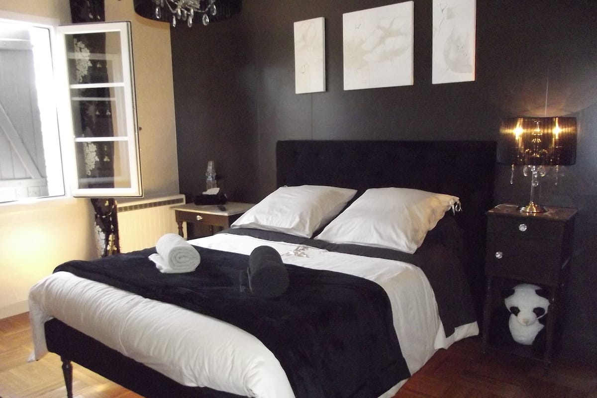 Ein Schlafzimmer mit einem schwarz-weißen Bett, einem Nachttisch mit Lampe und einem Fenster mit Vorhängen.