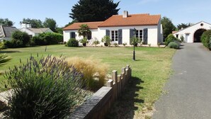 A white building with a red-tiled roof, surrounded by a well-maintained lawn and a wooden fence. - Entre Terre et Mer (Saint-Jean-de-Monts)