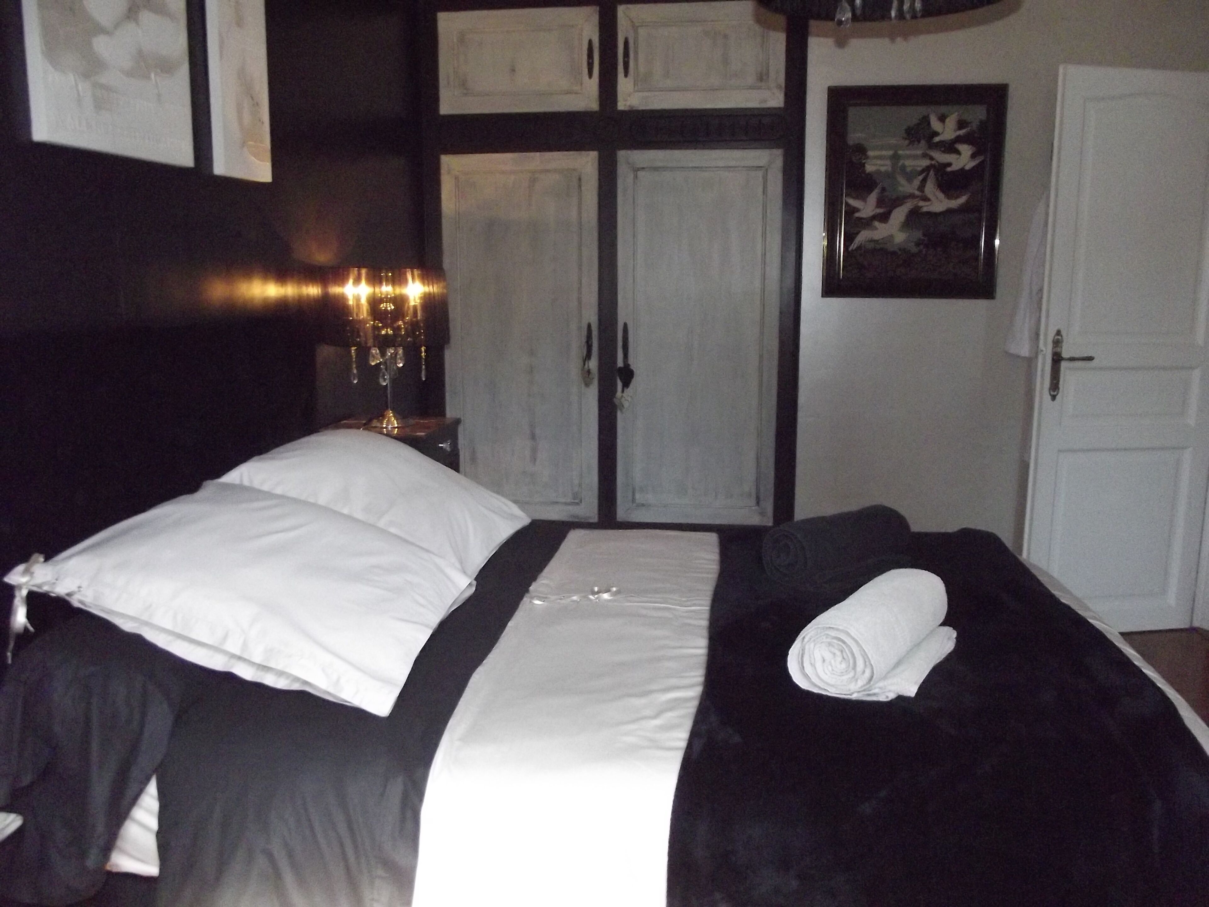 A bedroom with a bed, a nightstand, a lamp, a door, and a framed picture on the wall.