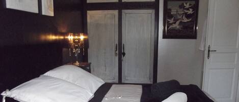 A bedroom with a bed, a nightstand, a lamp, a door, and a framed picture on the wall.