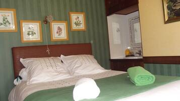 A neatly made bed with a green bedspread, white pillows, and a rolled green towel. There are four framed botanical prints on the wall above the bed.