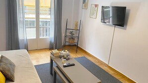A hotel room with a bed, a small table with items, a TV, and a balcony with curtains. - Check Point - Veikou (Athens)
