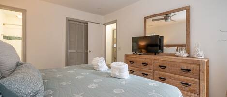 A bedroom with a bed, a wooden dresser, a television, and a ceiling fan.