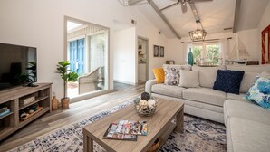 A spacious living room with a large television, a wooden coffee table, and a sofa with cushions. There is a ceiling fan and a window with a sailboat decoration. - 55 Lawton: Pet Friendly, Modern Luxury, Remodeled Sea Pines Home. Free Bikes (Hilton Head Island)