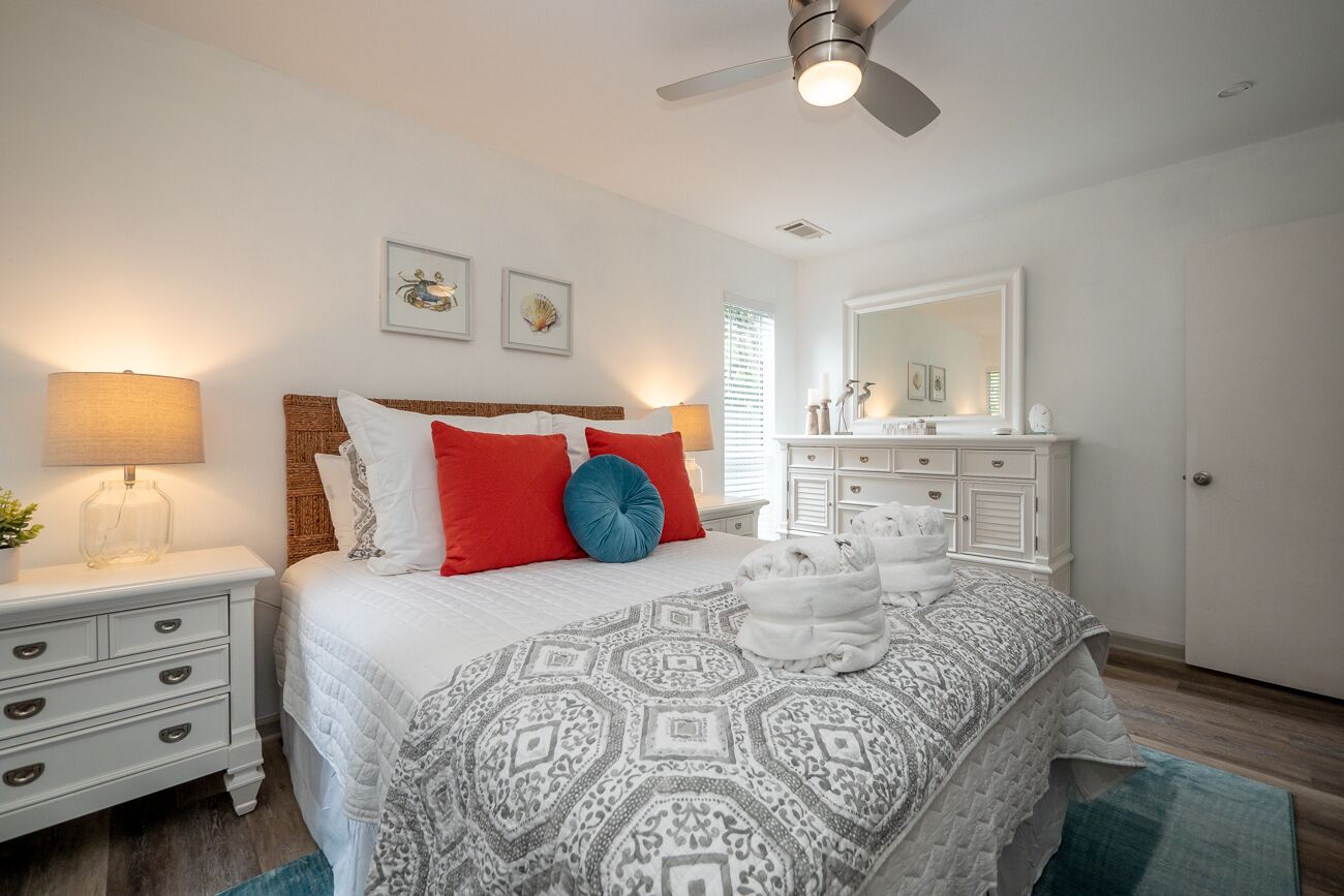 Une chambre à coucher comprenant un lit, des tables de chevet, une commode, un miroir et un ventilateur de plafond.