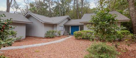 A residential property with a covered driveway, a blue garage door, and a well-maintained garden.