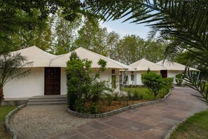 Une rangée de tentes blanches, avec un chemin pavé menant à elles, le tout entouré de verdure.
