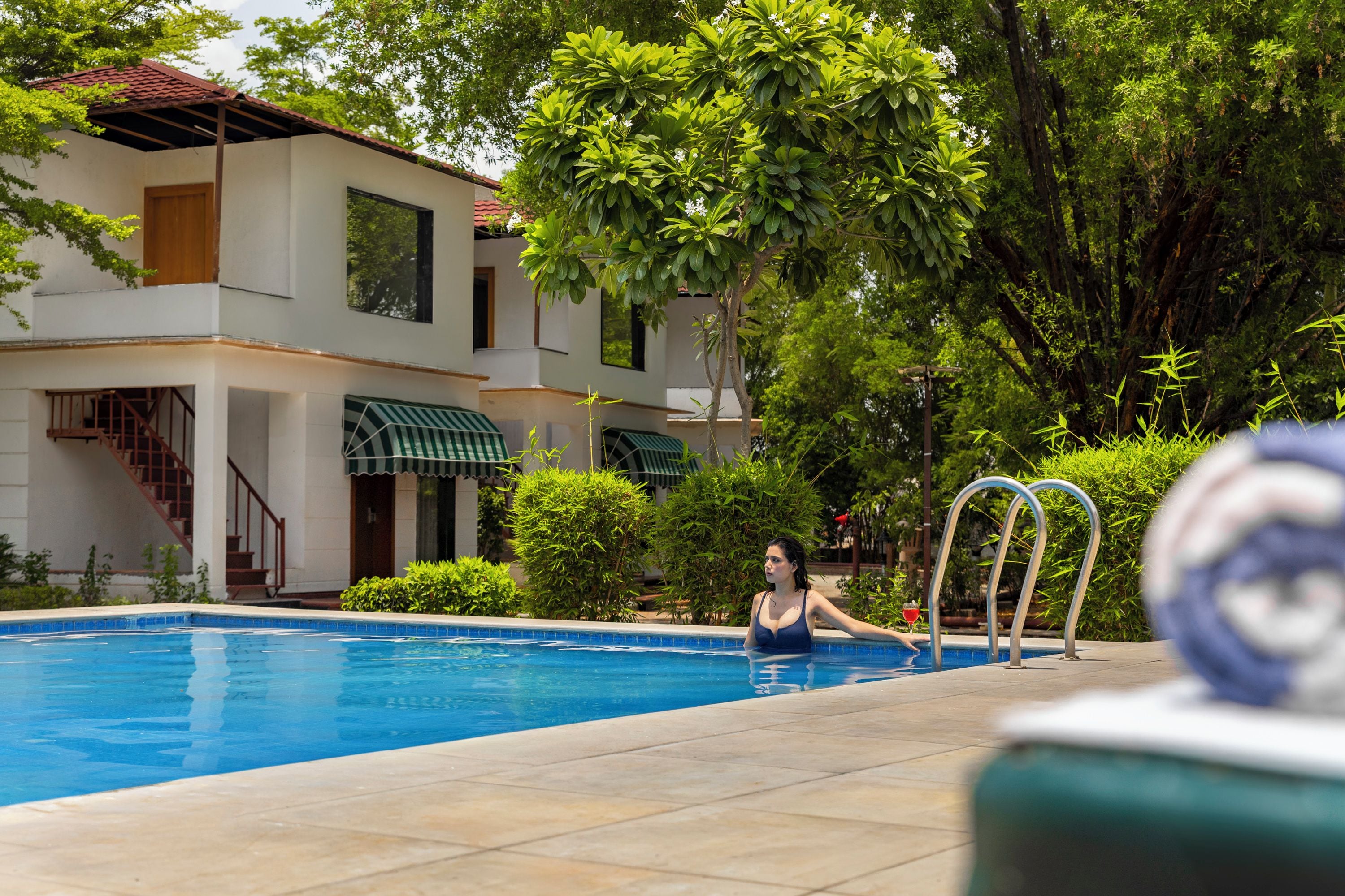 Una piscina con una persona dentro, rodeada de follaje y un edificio con tejado de cerámica.