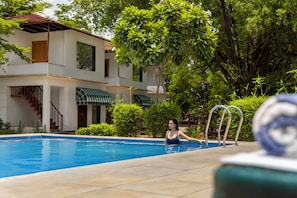 Una piscina con una persona dentro, rodeada de follaje y un edificio con tejado de cerámica.