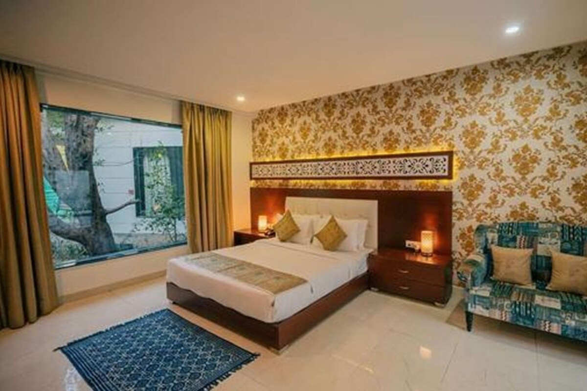 A bedroom with a large bed, a sofa, a nightstand, and a window with curtains.