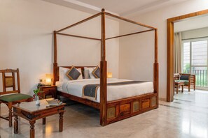 Una cama con dosel de madera y una silla tapizada de verde.