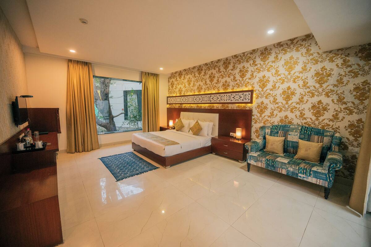 A hotel room with a bed, a sofa, a desk, and a large window with curtains.
