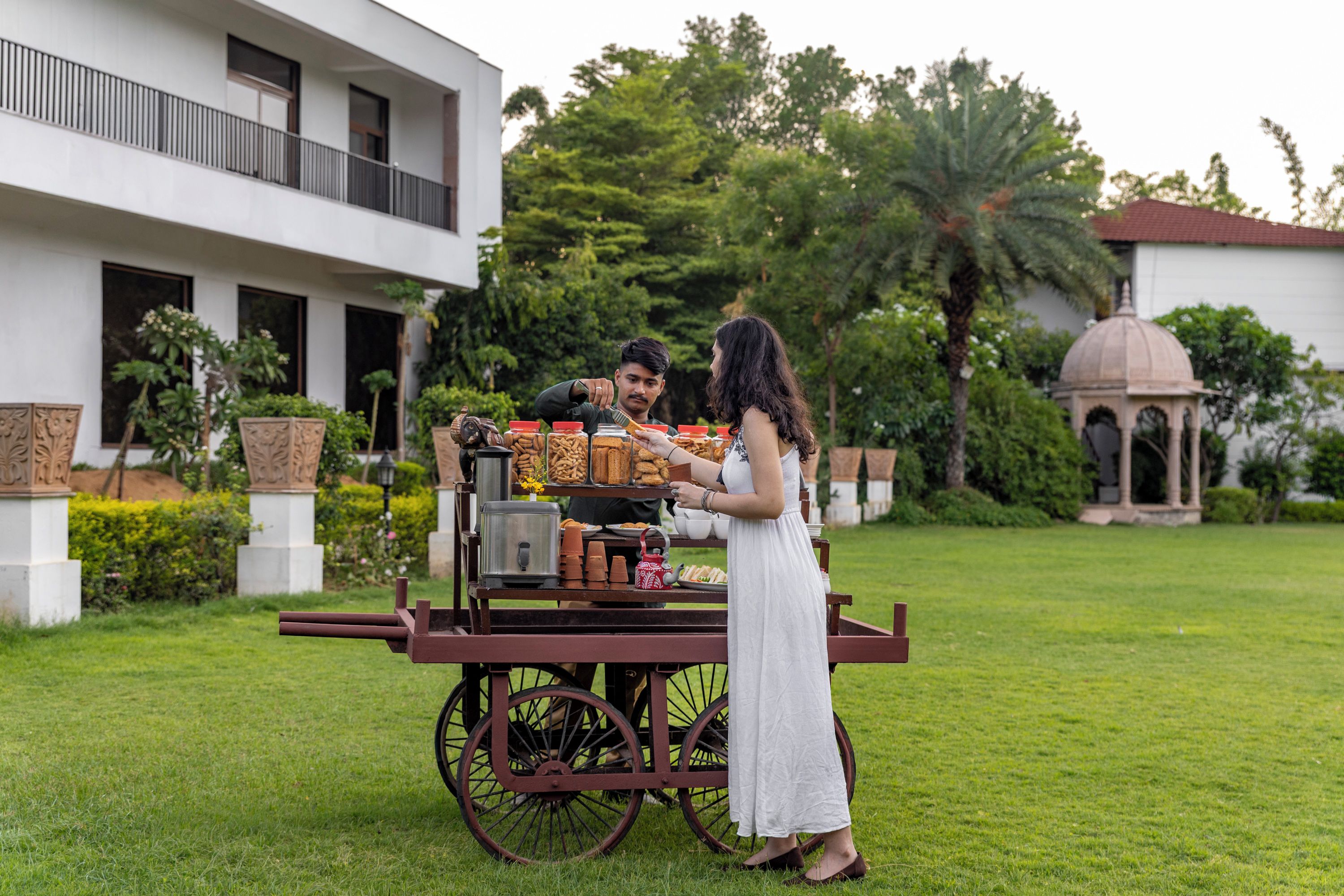 A cart with various food items in front of a building with a balcony and a dome structure in the background.
