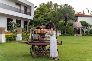 A cart with various food items in front of a building with a balcony and a dome structure in the background. - Tree of Life Tiger Trails, Ranthambore (Sawai Madhopur)