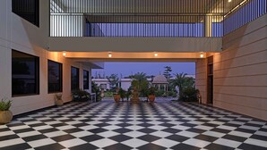 A checkered floor with a Buddha statue in the center, surrounded by potted plants, under a covered walkway with a view of a building with a dome in the background. - Tree of Life Tiger Trails, Ranthambore (Sawai Madhopur)