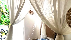 A bed with a blue and white striped bedspread, a white canopy, and a view of greenery outside. - 2Gites 800m from the beach private swimming pool in a tropical setting (Deshaies)