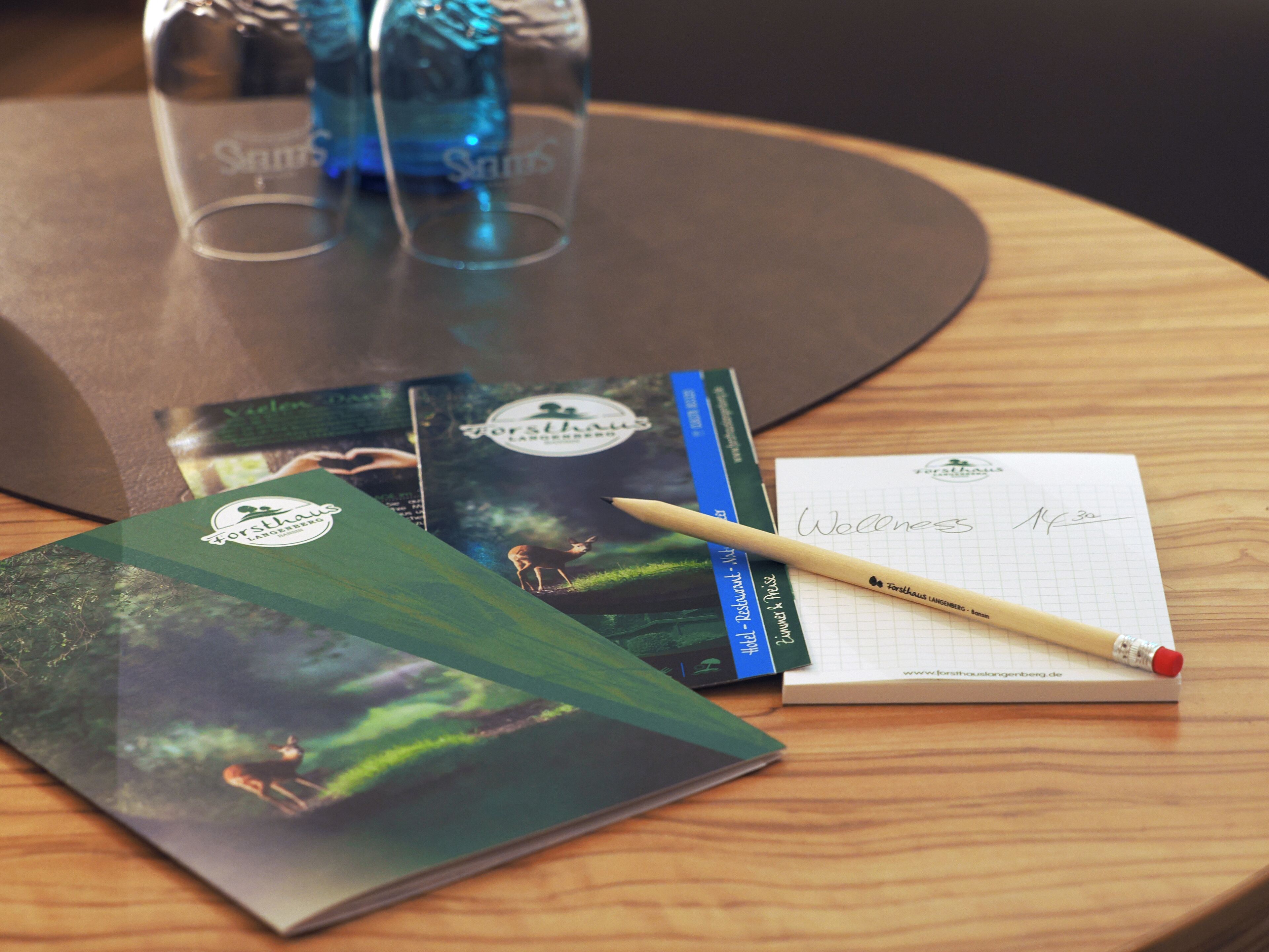 A notebook, a pen, and two books on a wooden table.