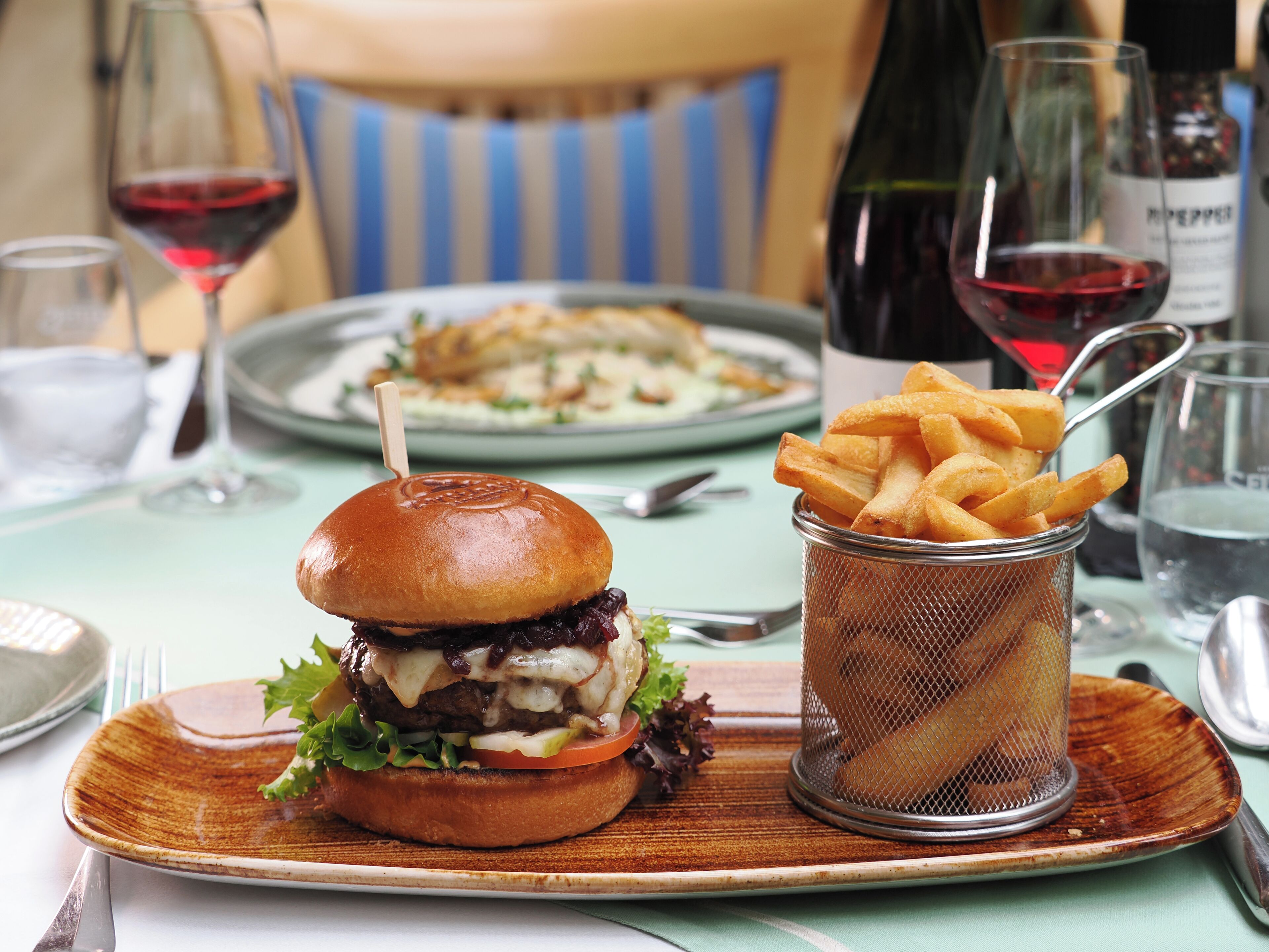 A meal with a burger, fries, and a glass of red wine on a table.