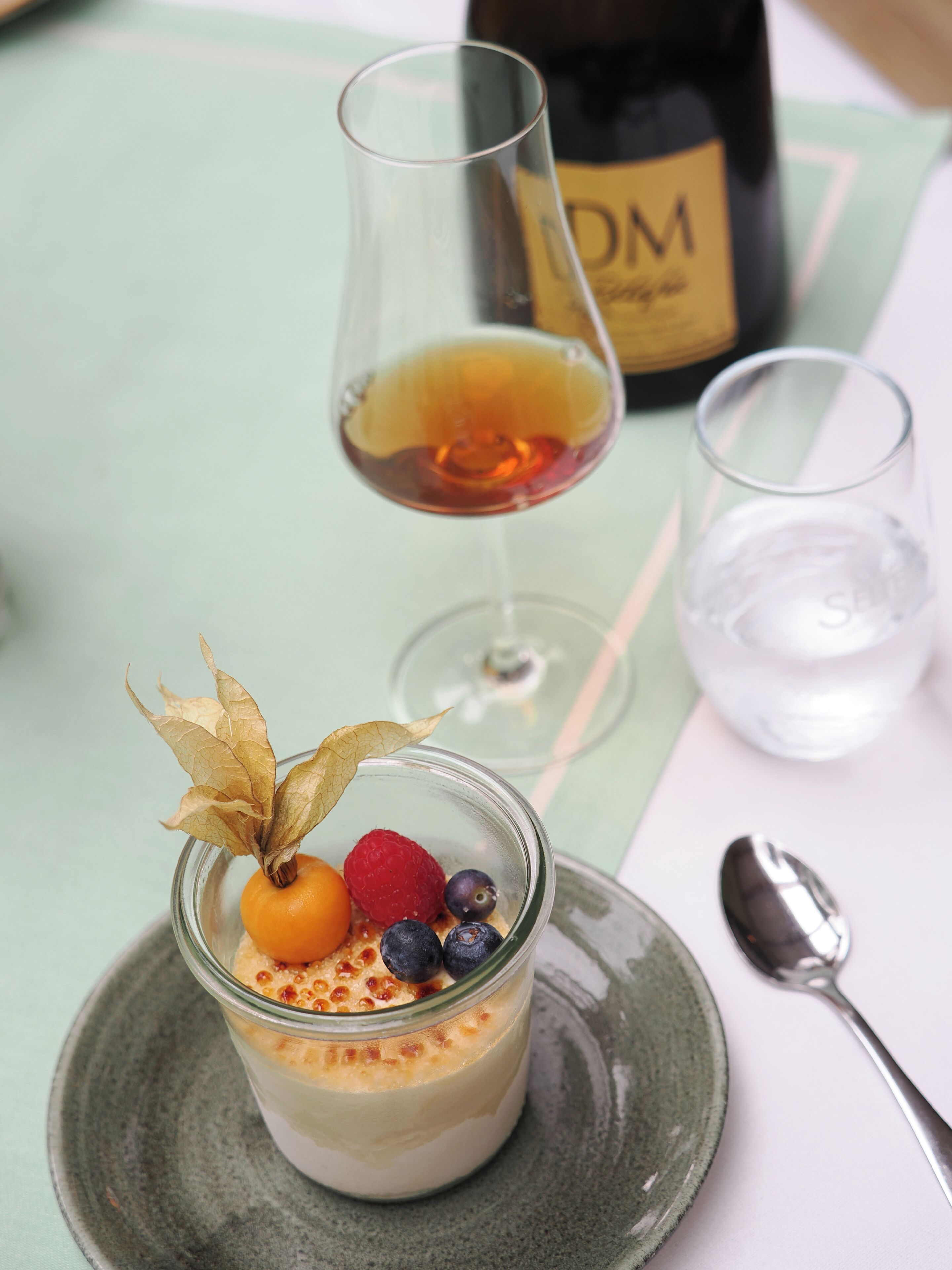 A dessert in a glass, a bottle, and a spoon on a table.