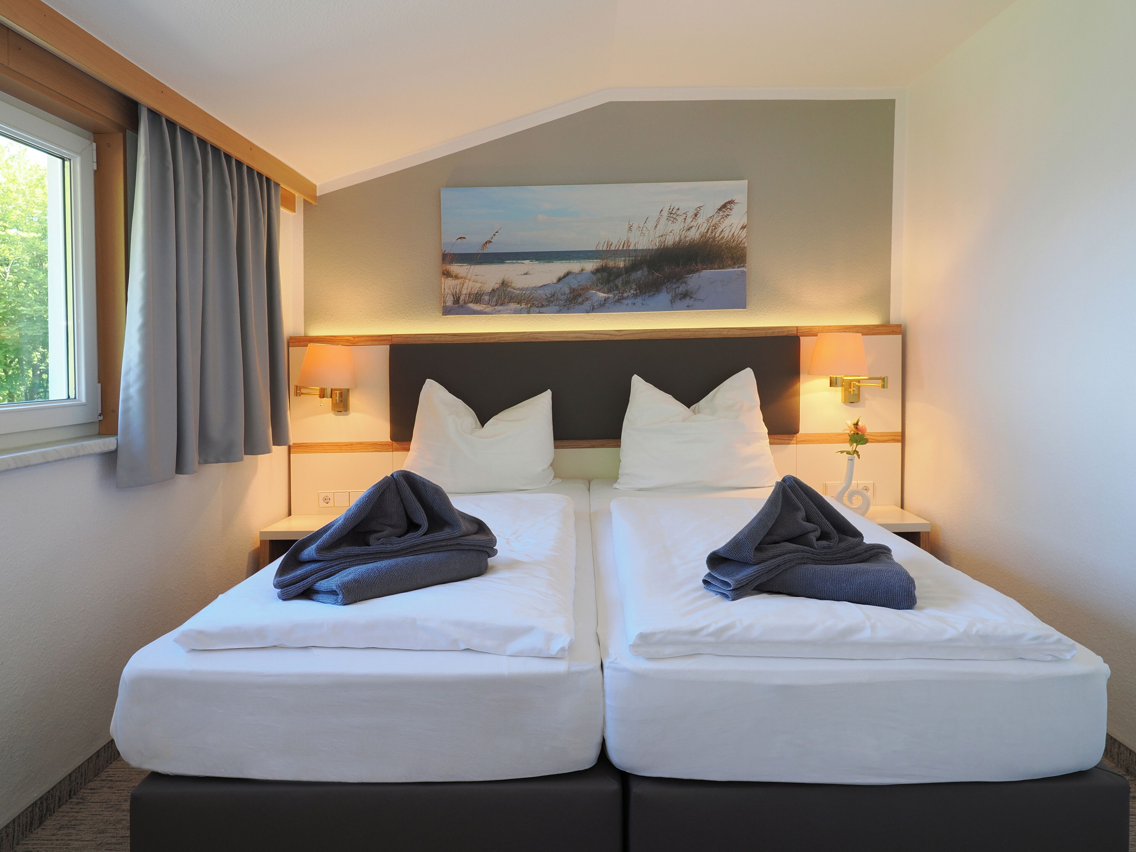 A hotel room with two beds, a painting of a beach scene, and bedside lamps.