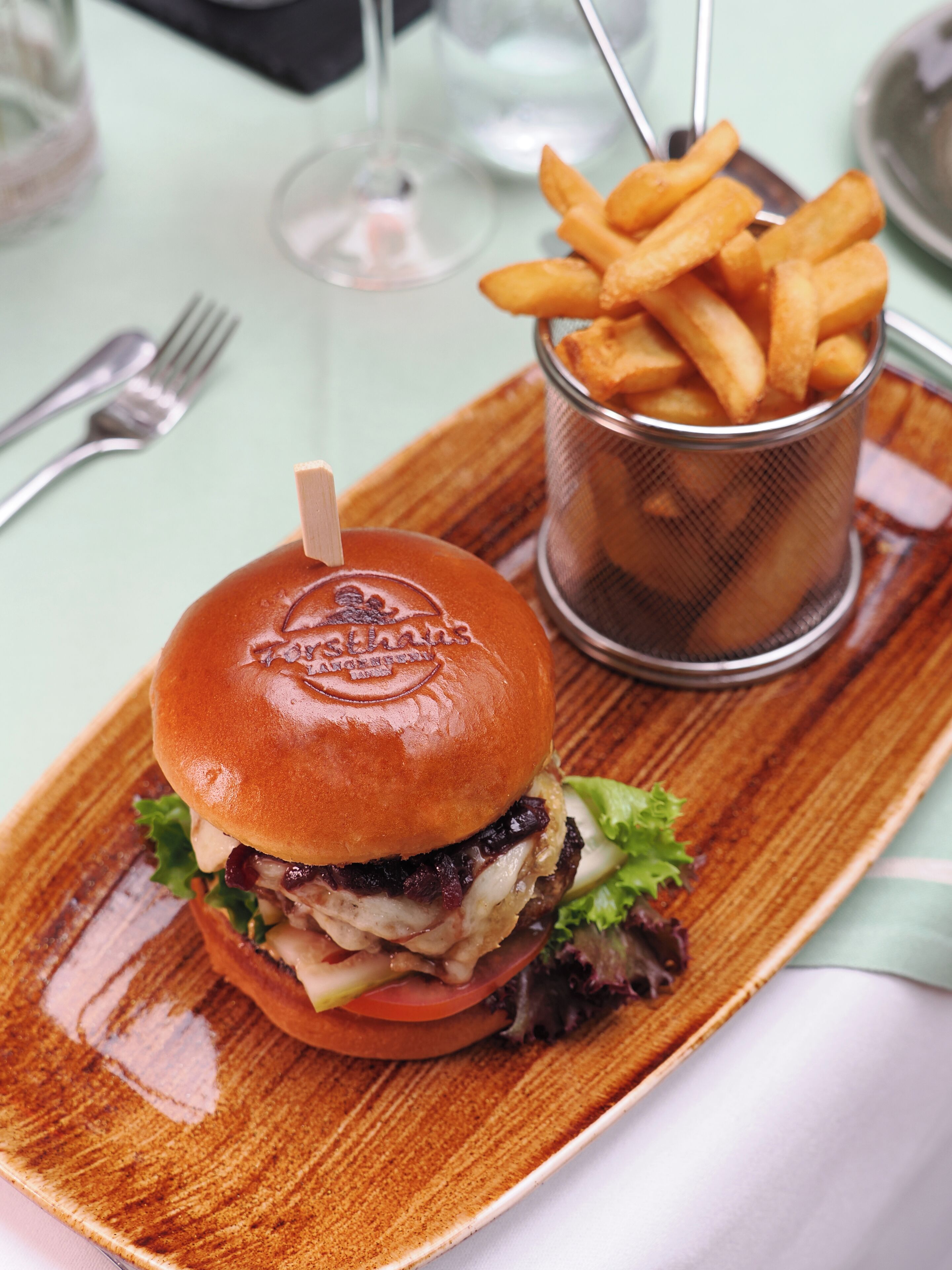Un sándwich sobre una tabla de madera con papas fritas en un cesto de metal.