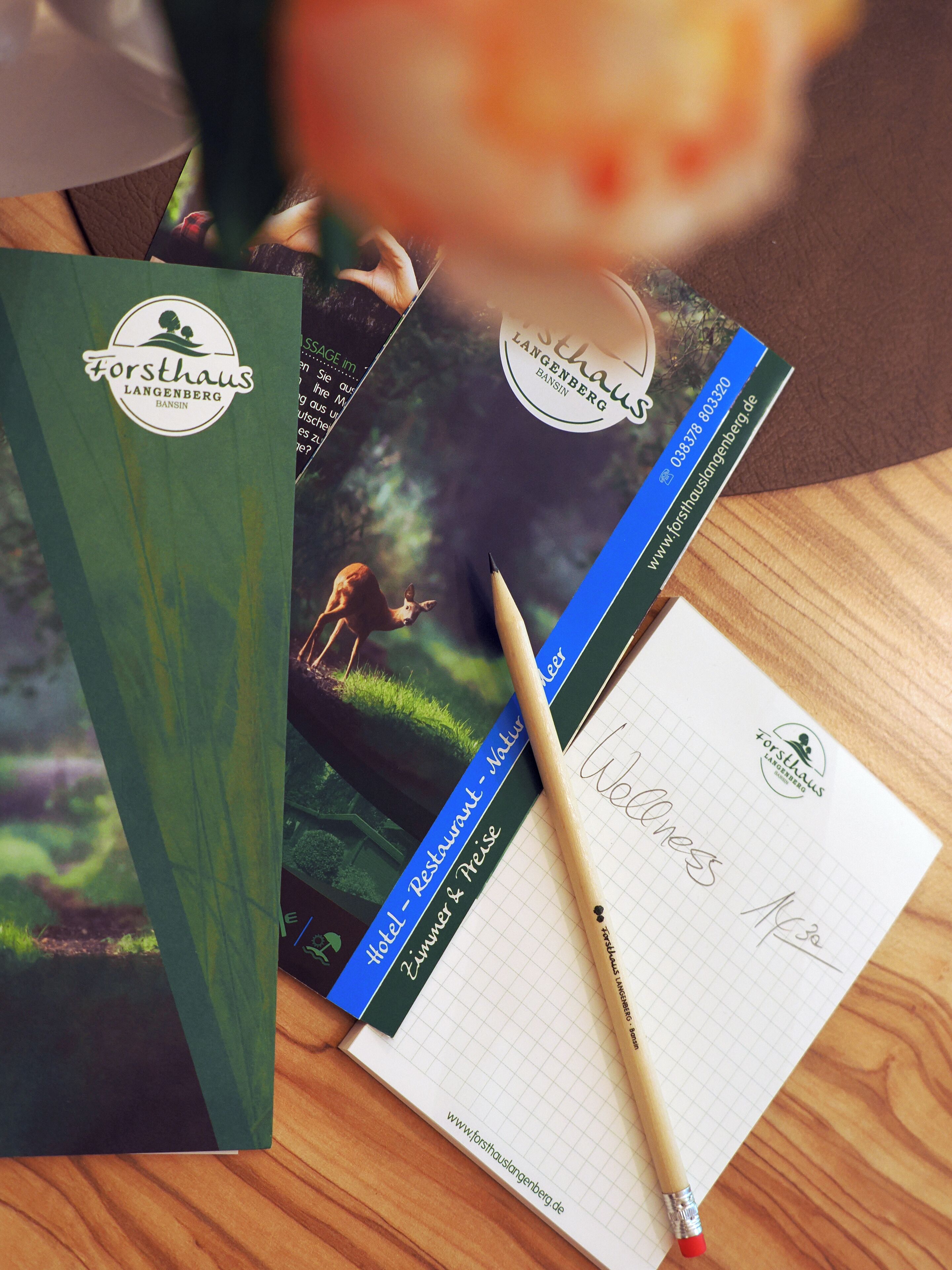 Un cuaderno con un bolígrafo, un folleto y una carpeta verde con el logo "Forsthaus Langenberg".