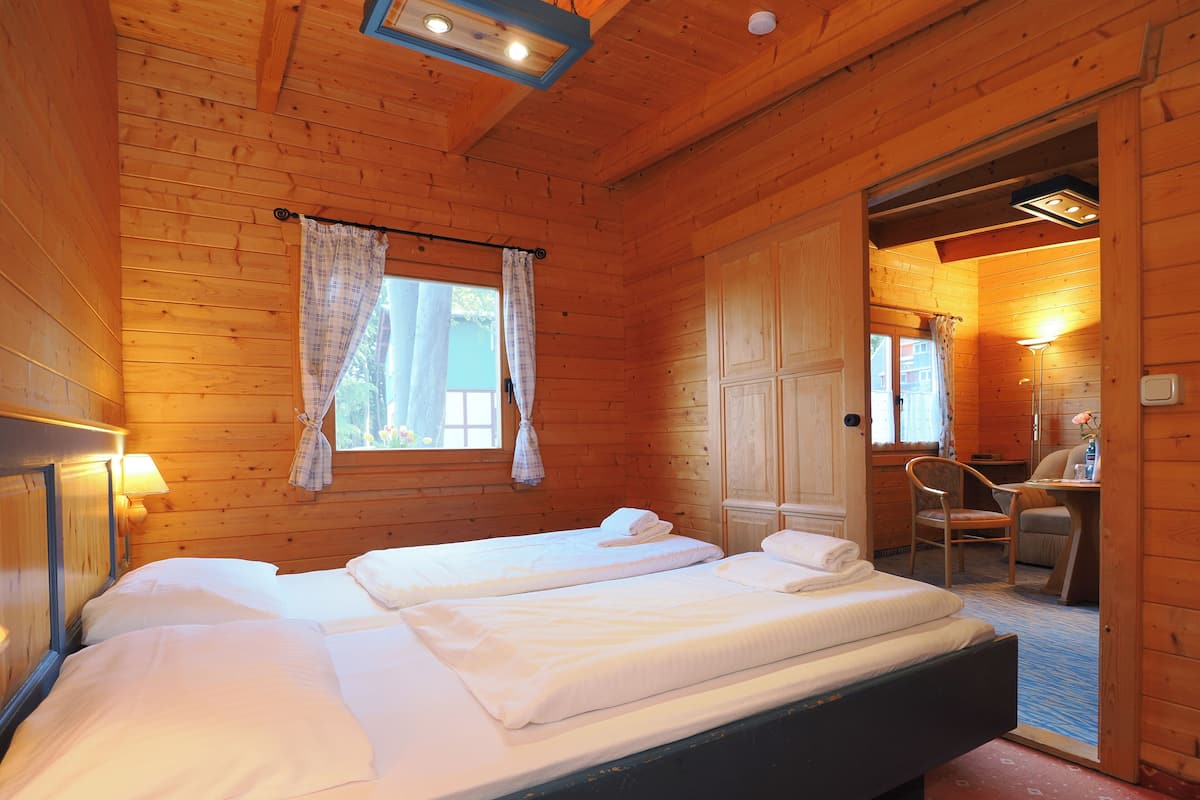 A wooden cabin room with two beds, a desk, and a chair.