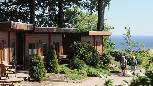 Una cabaña de madera con un porche, mobiliario exterior y vistas al mar.