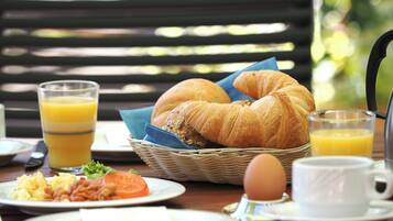 A breakfast table with croissants, a basket, a glass of orange juice, a plate of eggs, and a cup of coffee.
