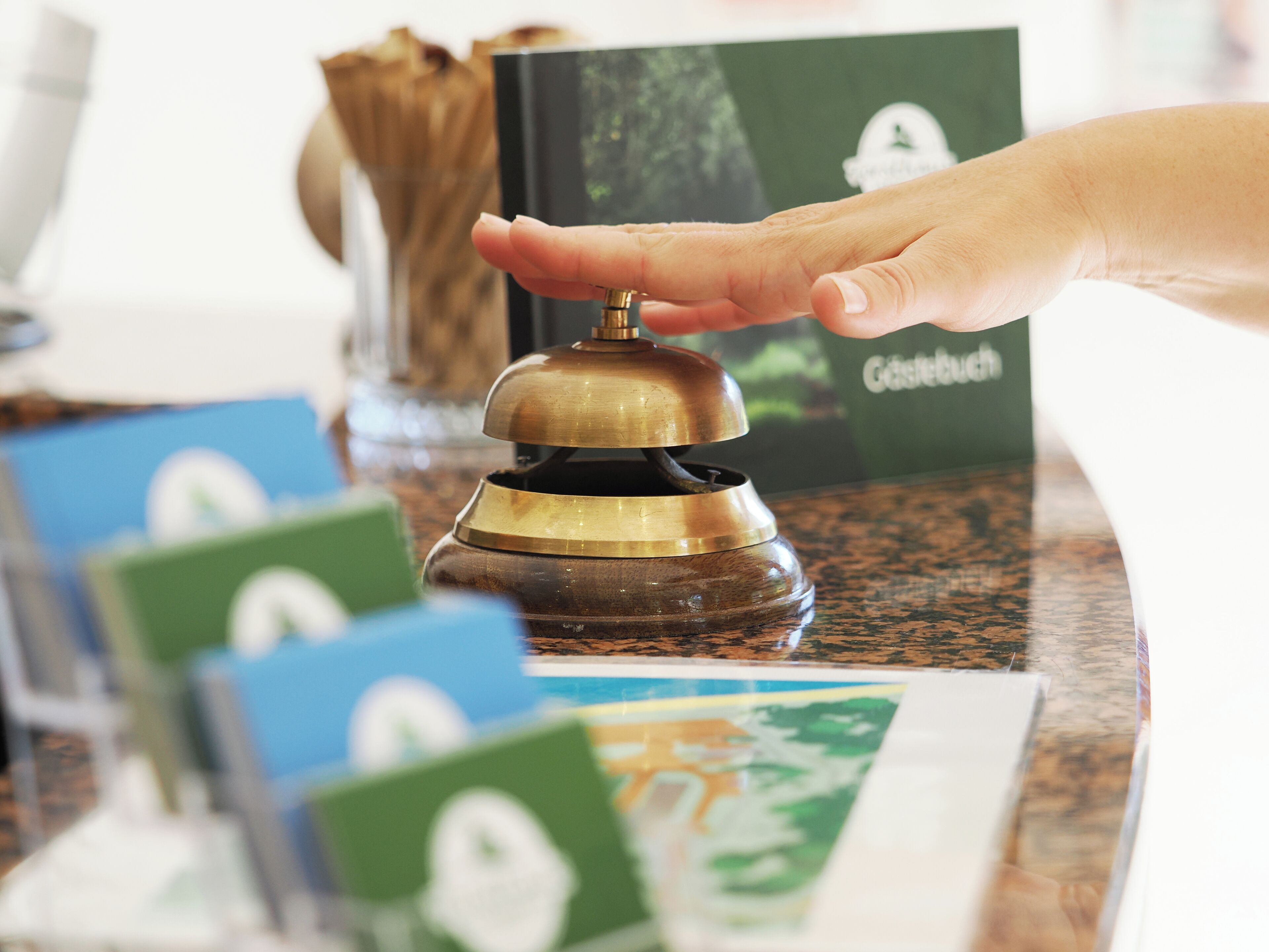 A hand pressing a brass bell on a wooden counter with a green and white card in front.