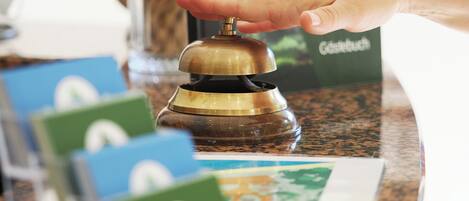 A hand pressing a brass bell on a wooden counter with a green and white card in front.