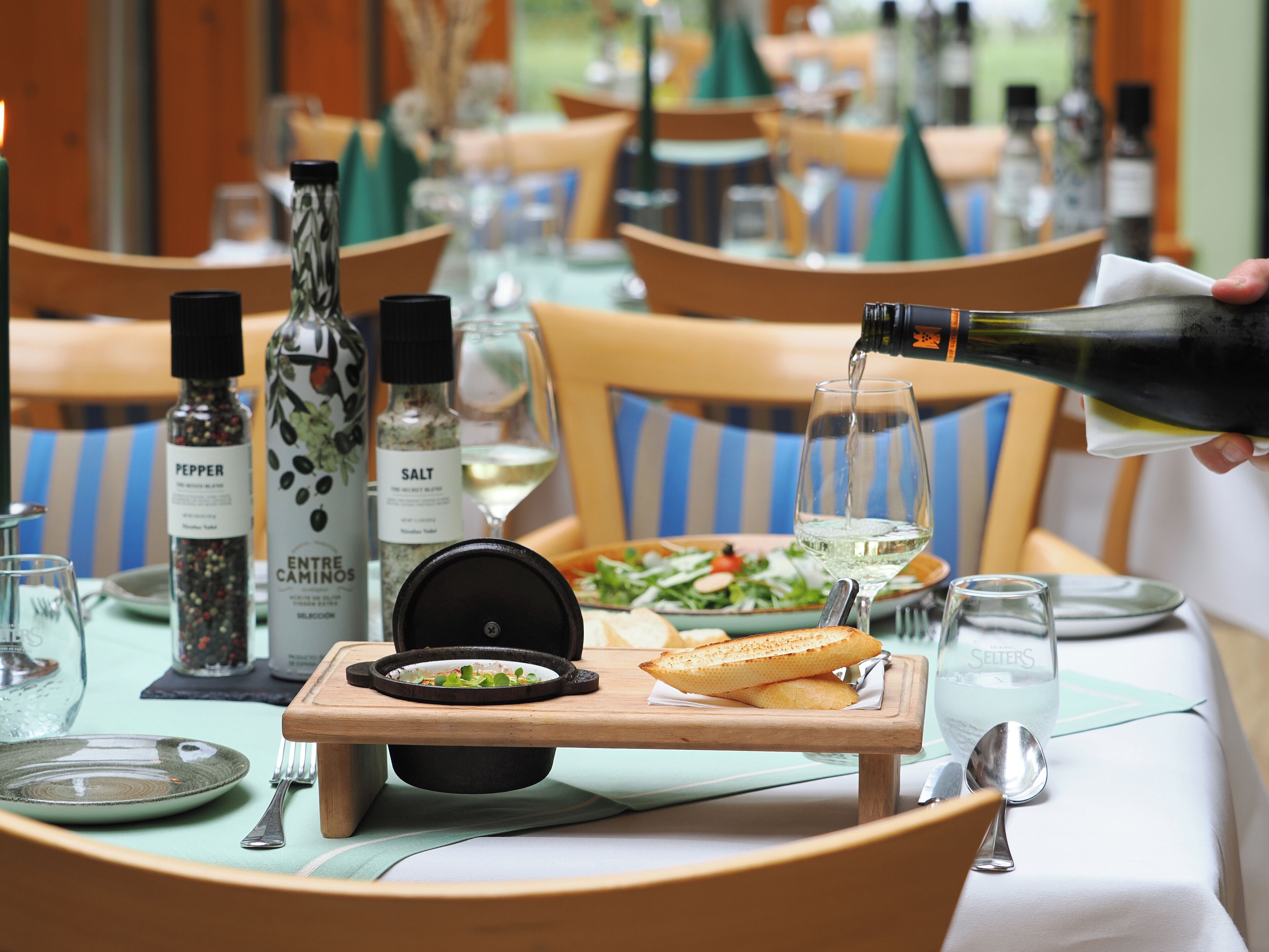 A dining table set with plates, cutlery, a bottle of water, a bottle of wine, and a bottle of pepper.