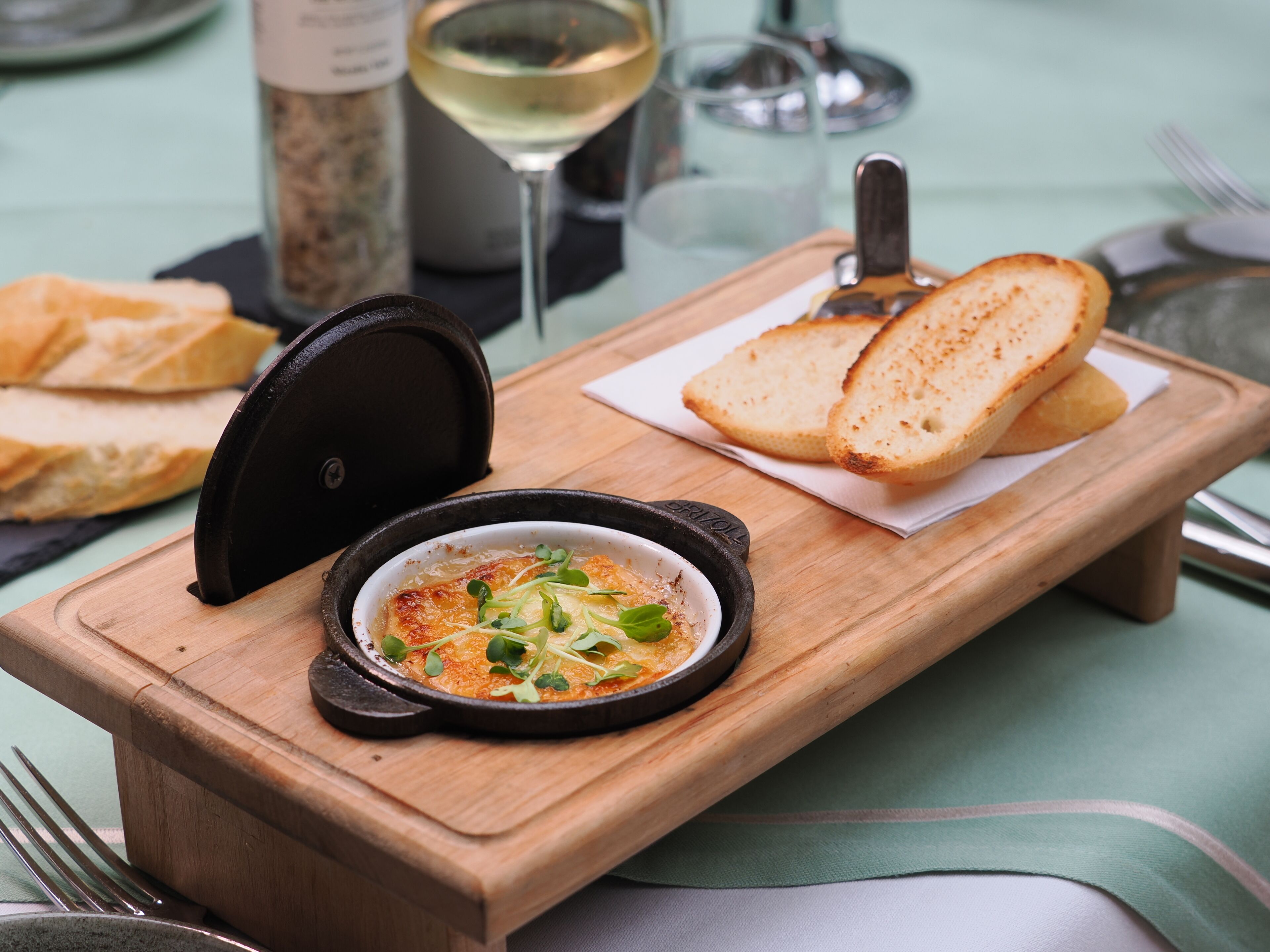 A wooden serving board with a bowl of food, two slices of bread, and a wine glass.