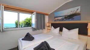 Habitación de hotel con dos camas, un ventanal con vista al mar y un cuadro en la pared.