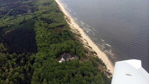 Vista aérea de una zona costera con bosque denso, una playa de arena y un pequeño edificio con paneles solares.
