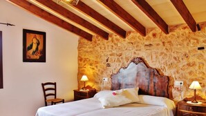A bedroom with two beds, stone walls, wooden beams, and a painting on the wall. - Rural estate with pool and professional tennis court (LLucmajor)