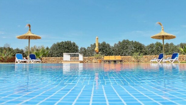 A swimming pool with lounge chairs and umbrellas, surrounded by a stone wall and greenery. - Rural estate with pool and professional tennis court (LLucmajor)