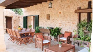 A stone patio with wooden furniture, including a table and chairs, and potted plants. - Rural estate with pool and professional tennis court (LLucmajor)