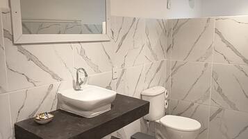 A modern bathroom with a white sink, dark countertop, and marble-patterned walls.