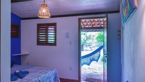 Une chambre avec deux lits, une fenêtre avec des volets et une porte donnant sur un espace extérieur équipé d’un hamac.