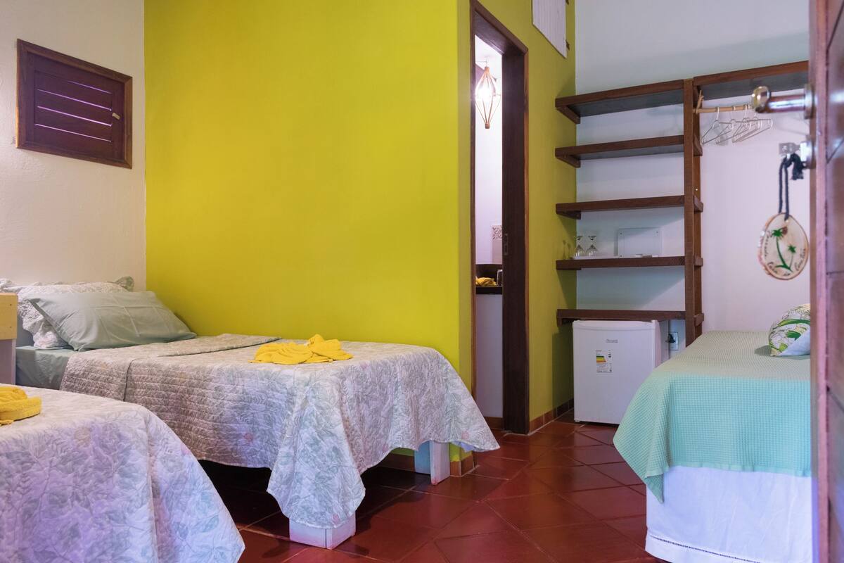 Ein Zimmer mit zwei Betten, einem kleinen Kühlschrank und einem Regal mit hängenden Gegenständen.