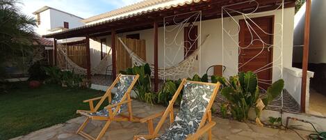 A patio with two wooden lounge chairs, a hammock, and a stone-tiled floor.