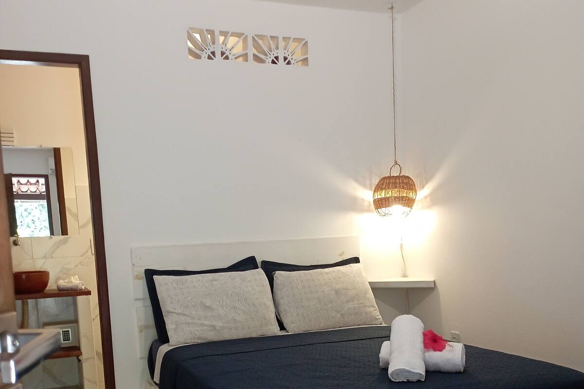 Ein Schlafzimmer mit Bett, Kissen, Nachttisch, Lampe und einer Wandleuchte.