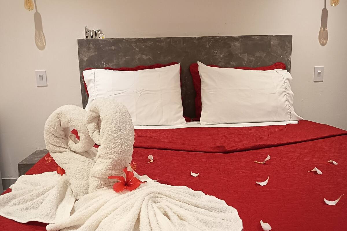 Ein ordentlich bezogenes Bett mit roter Bettdecke, weißen Kissen und einer dekorativen Handtuchgestaltung.