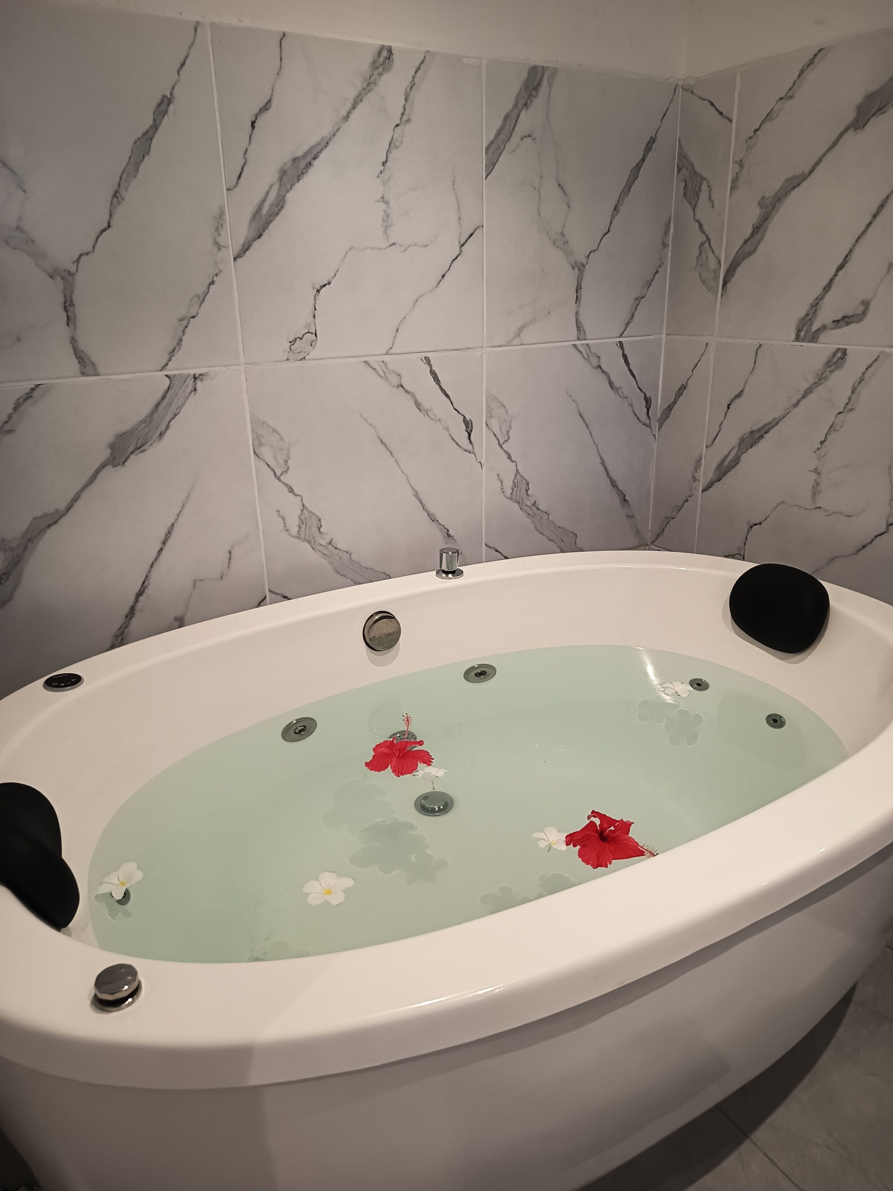 Una bañera con agua y flores, baldosas en la pared con diseño de mármol y una bañera blanca.