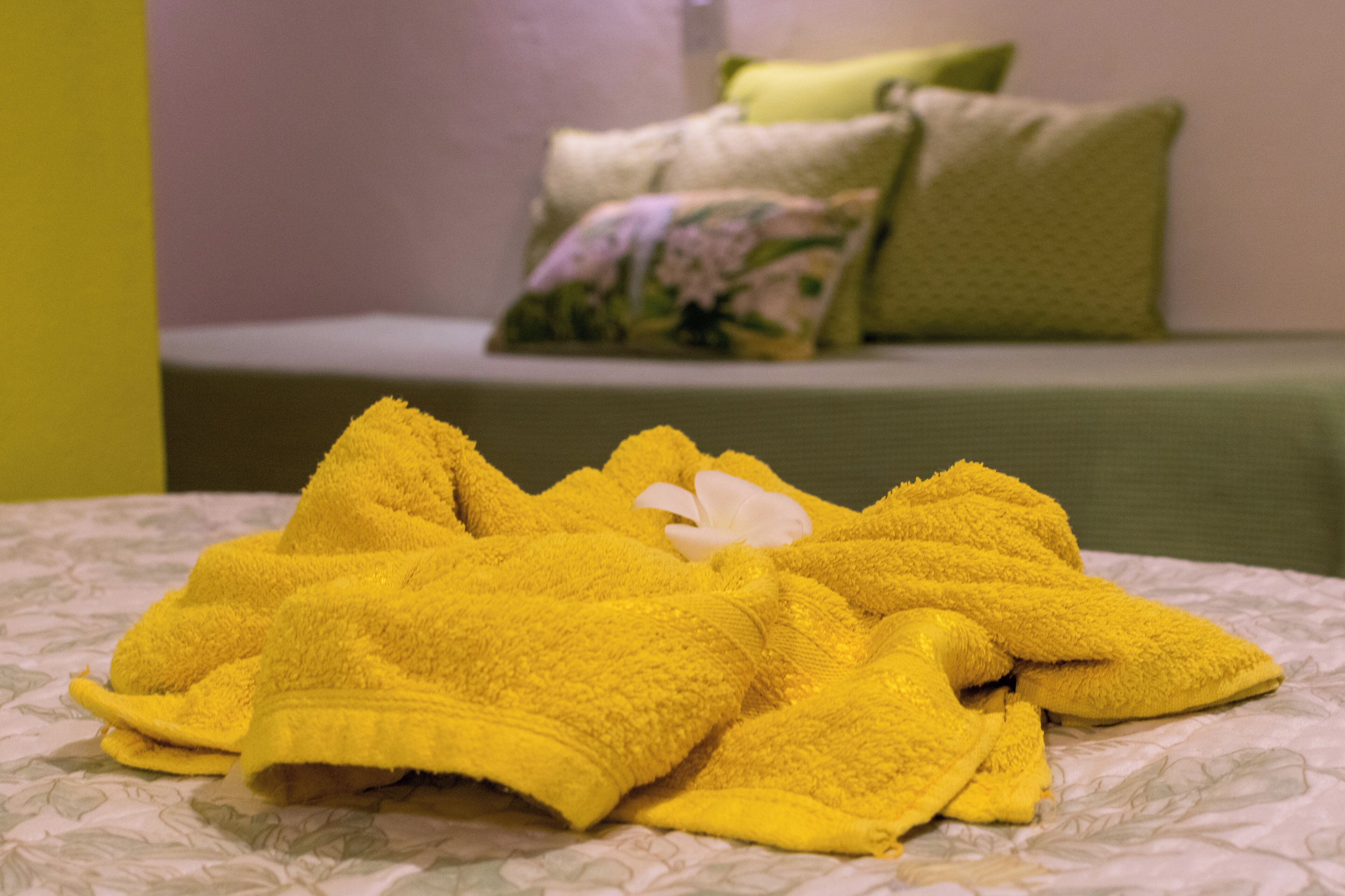A bed with a floral-patterned bedspread and a yellow towel on it.